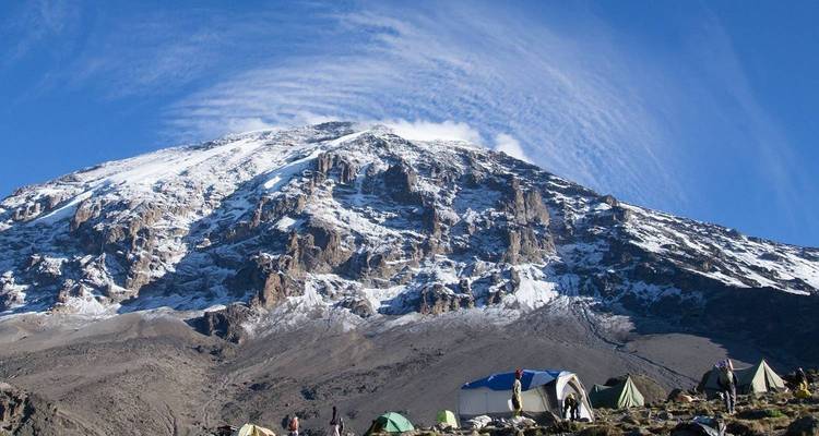 Campamento alpino con tiendas de campaña ubicado bajo la cara escarpada y nevada del Kilimanjaro.