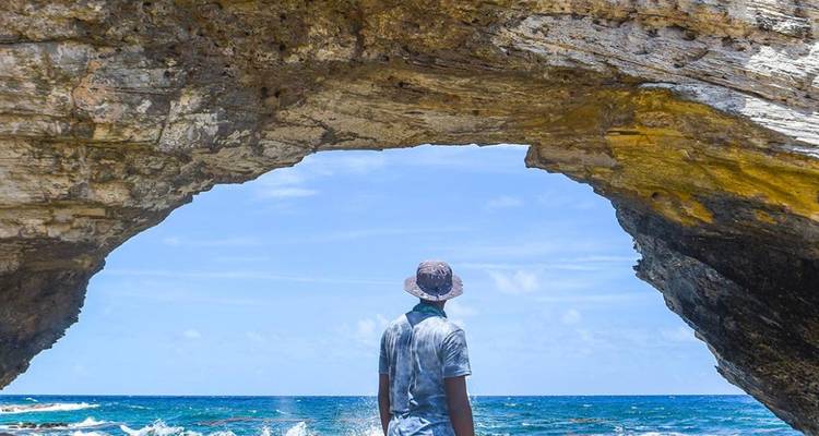 Personne debout sous une arche rocheuse, regardant vers la mer.