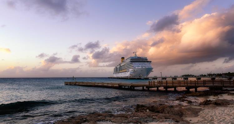 Navire de croisière amarré près d'un littoral pittoresque au coucher du soleil.