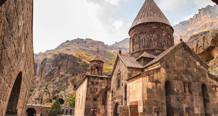 Iglesia histórica de piedra del Monasterio de Geghard situada contra montañas escarpadas teñidas de otoño.
