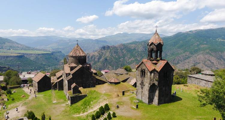Complejo monasterio medieval en la cima de una colina con campanario rodeado de valles verdes montañosos.