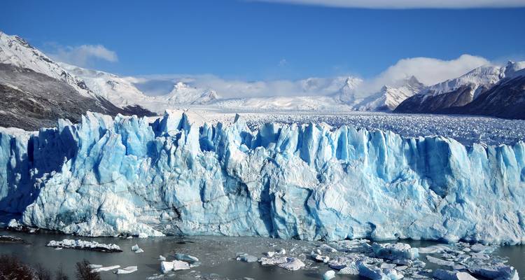 Gran glaciar con formaciones azul hielo y montañas al fondo.
