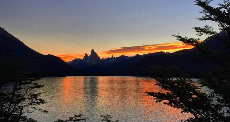 Vista del atardecer sobre un lago con montañas y un cielo naranja.
