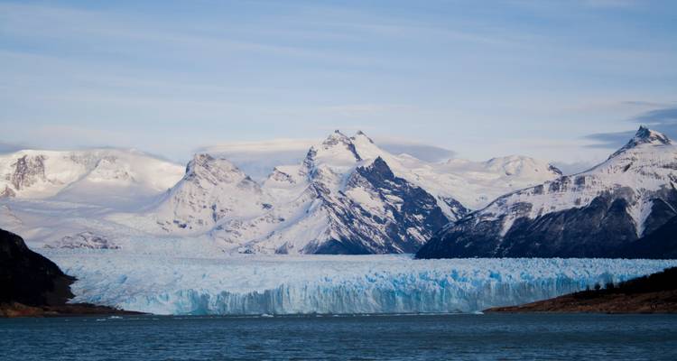 Montañas cubiertas de nieve detrás de un glaciar masivo y una masa de agua tranquila.