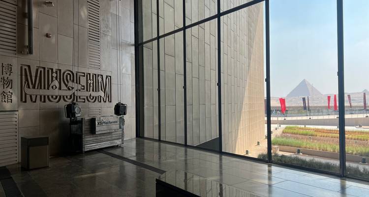 Interior de museo moderno con gran ventanal con vista a una pirámide.