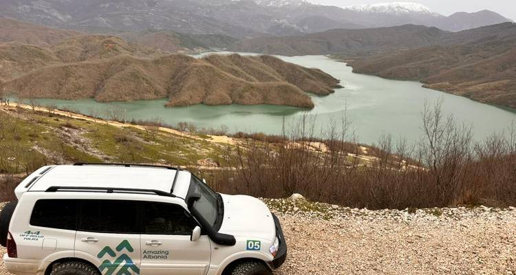 SUV avec la marque 'Amazing Albania' garé au-dessus d'un réservoir vert et d'îlots arides.