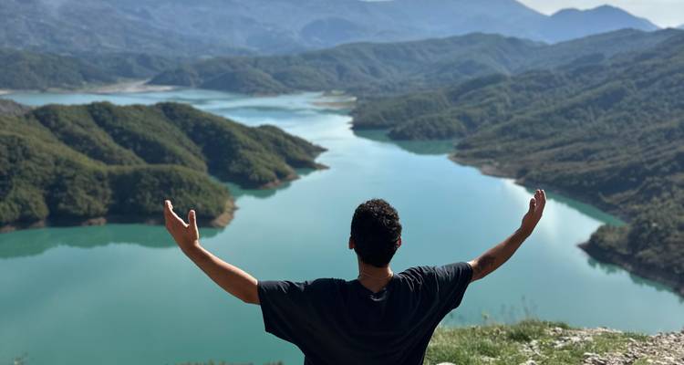 Un voyageur lève les bras en signe de triomphe en contemplant un lac de montagne éclatant en Albanie.