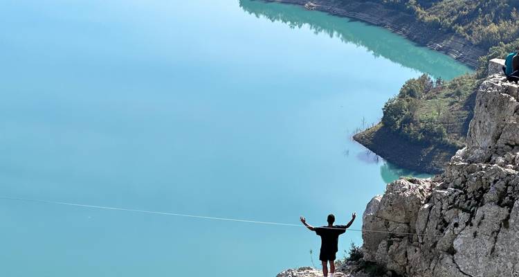 Une petite silhouette se dresse sur une falaise au-dessus d'un réservoir turquoise comme un miroir, les bras étendus.