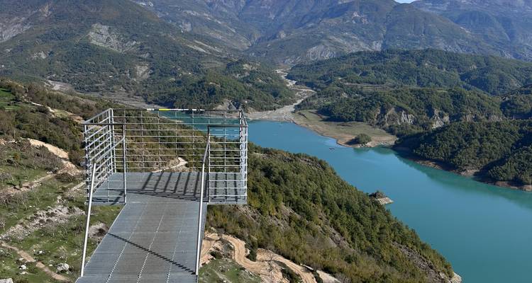 Plateforme d'observation métallique qui s'avance au-dessus d'une vallée profonde et d'un réservoir bleu dans les montagnes albanaises.