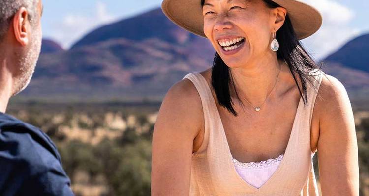 Happy traveler laughing outdoors with arid Australian landscape and domed hills in soft focus behind.
