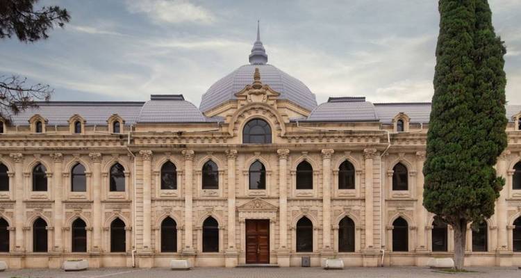 Bâtiment gouvernemental historique en pierre beige avec des fenêtres cintrées et un grand cyprès en Azerbaïdjan.
