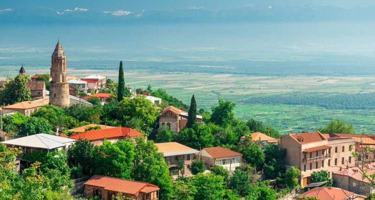 Ville géorgienne perchée sur une colline avec un clocher d'église et des toits en terre cuite surplombant une vaste plaine et des montagnes brumeuses au loin