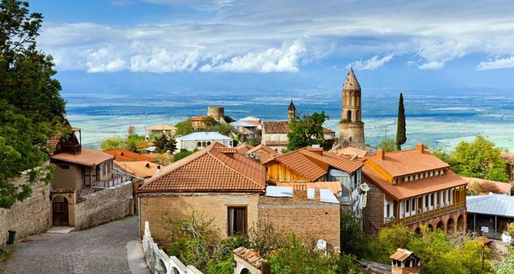 Ville médiévale pittoresque perchée sur une colline avec des tours de pierre, des maisons aux toits rouges et des vues panoramiques sur les terres agricoles et les montagnes enneigées du Caucase