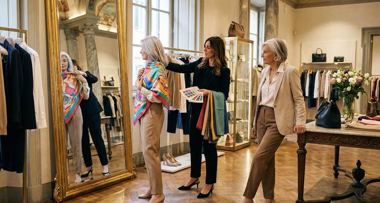 Deux femmes mûres reçoivent des conseils de mode tout en essayant des foulards dans une boutique élégante avec de grands miroirs.