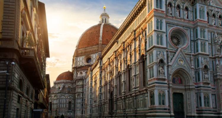 Le Duomo emblématique de Florence et le Baptistère brillent dans la lumière chaude du lever du soleil le long d'une rue étroite de la ville.