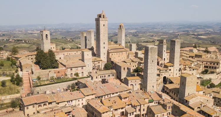 Vue de drone des tours de pierre médiévales de San Gimignano s'élevant au-dessus de la campagne toscane vallonnée.