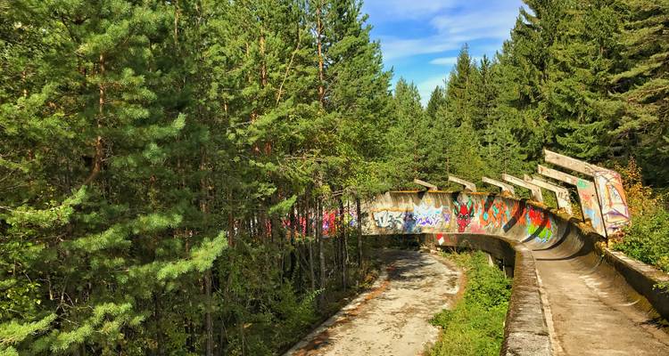 Piste de bobsleigh abandonnée couverte de graffitis à travers une forêt.