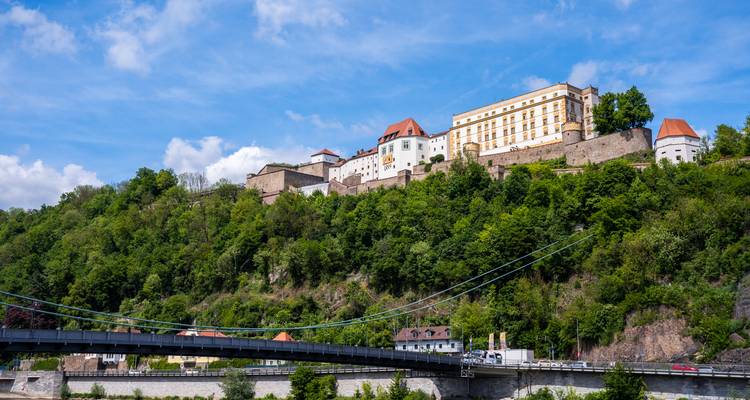 La forteresse Veste Oberhaus de Passau au sommet d'une colline boisée avec un pont moderne traversant le Danube en contrebas.