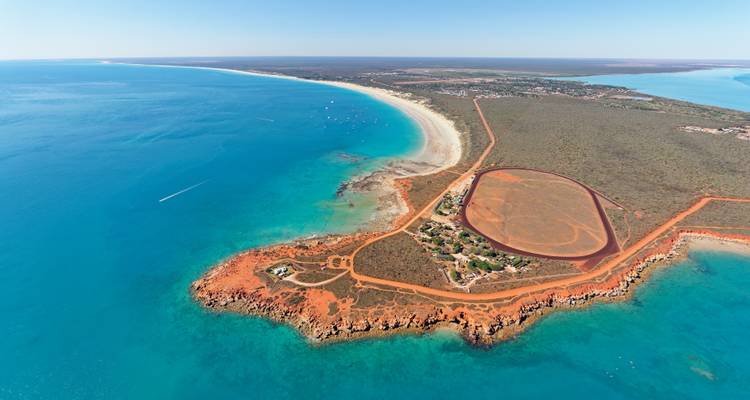 Spectacular aerial of red-cliff peninsula and turquoise waters surrounding Broome’s Cable Beach.