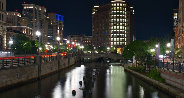 Vue nocturne des immeubles de la ville reflétés dans un canal avec des ponts illuminés et des lampadaires à Providence.