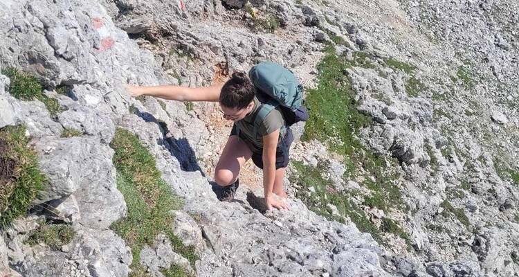 Vrouwelijke wandelaar die haar handen gebruikt om een steile rotsrichel in de Dolomieten te beklimmen