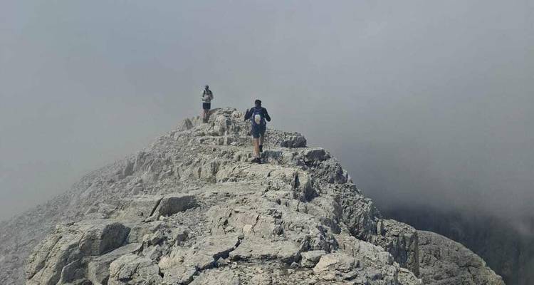 Twee wandelaars die langs een smalle rotsachtige bergkam lopen en verdwijnen in de mist