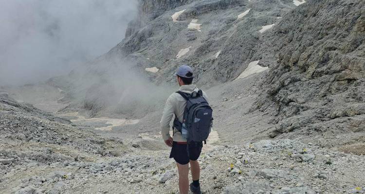 Wandelaar staand op een puinhelling uitkijkend over een met mist gevulde alpenkom