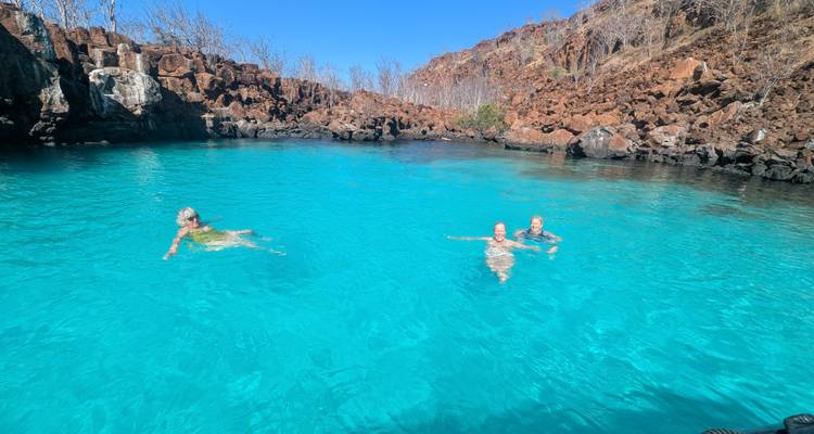 Trois personnes nageant dans un lagon bleu entouré de falaises rocheuses.