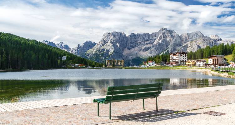 Banc surplombant un lac alpin serein avec forêt et pics calcaires se reflétant dans l'eau