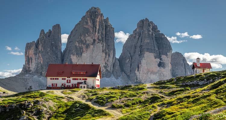 Pics emblématiques des Tre Cime di Lavaredo avec refuges alpins et sentiers verdoyants vallonnés sous un ciel dégagé