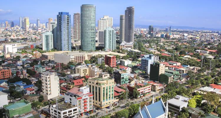 Weites Tagespanorama eines dicht bebauten Stadtgebiets mit Hochhäusern, die sich über bunte niedrige Wohnviertel erheben.