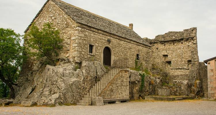 Stenen kapel ingebouwd in een rotsformatie met verweerde muren, externe trap en bewolkte lucht erboven.