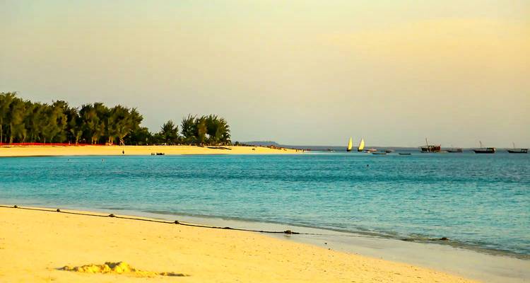 Plage tropicale tranquille avec eau turquoise, sable blanc et boutres naviguant au loin à l'heure dorée