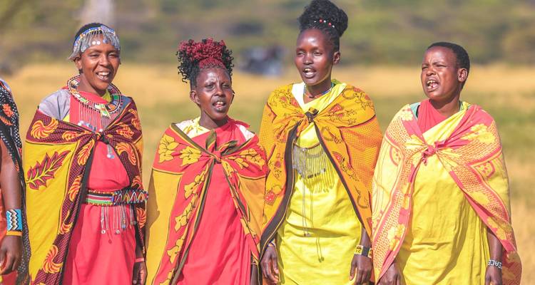 Des femmes maasaï en shukas jaune et rouge vives chantent dans une prairie ouverte en plein jour