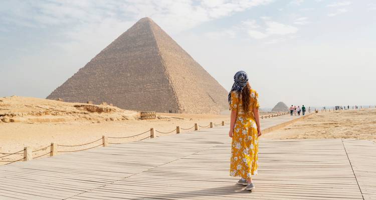 Persona caminando hacia la Gran Pirámide de Giza por un sendero de madera.