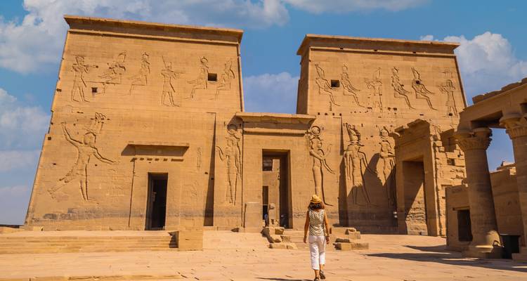 Individuo caminando hacia un templo del antiguo Egipto bajo un cielo azul.
