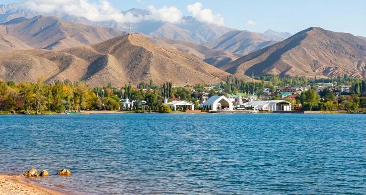 Een groot blauw meer met grasrijke oevers en verre bergen onder een heldere hemel.