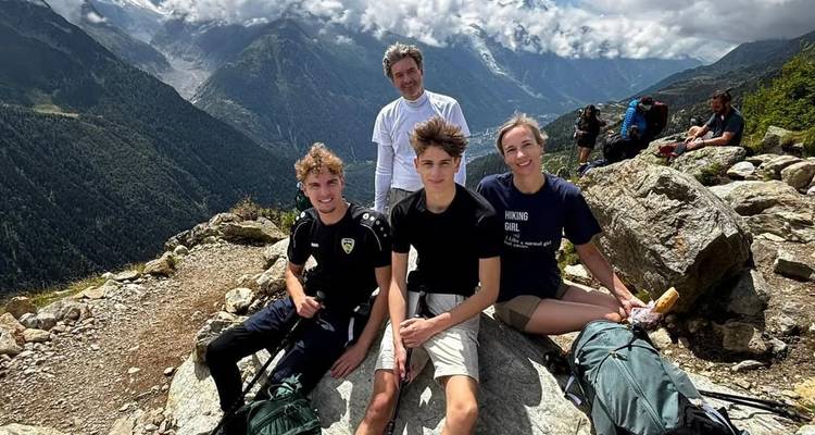 Quatre randonneurs souriant en se reposant sur un rocher avec des pics alpins spectaculaires derrière eux.