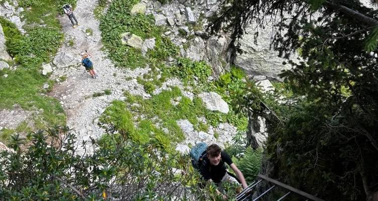 Des randonneurs vus d'en haut gravissant une échelle métallique sur un sentier alpin rocheux.