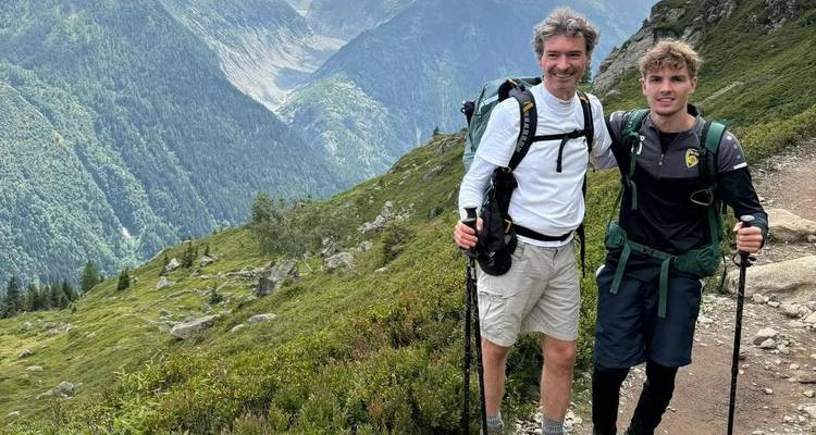Deux randonneurs avec des bâtons de marche posant sur un sentier de montagne surplombant une vallée profonde.