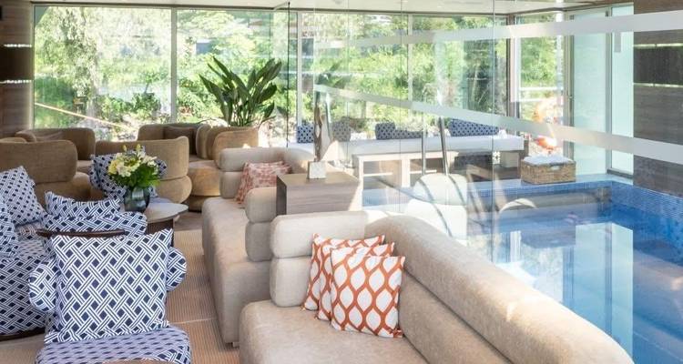 Binnen loungeruimte met kleurrijke zitplaatsen, glazen zwembad en groene planten.
