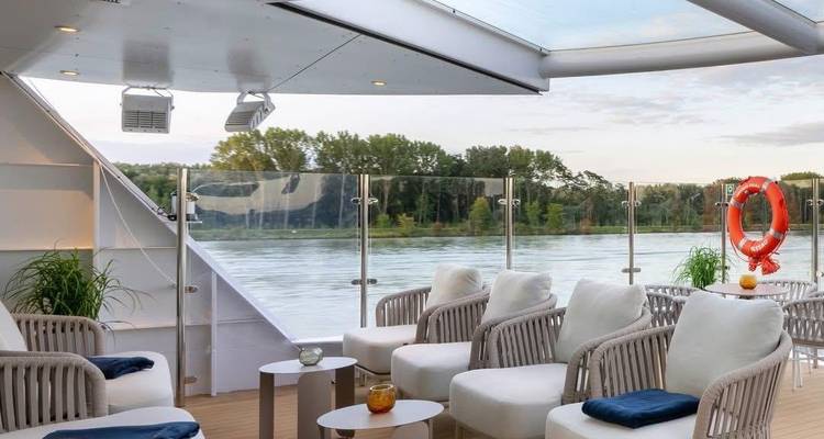 Gezellige zithoek op het dek van een schip, met uitzicht op rivier en heuvels.