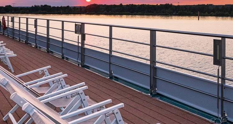 Scheepsdek ingericht voor ontspanning tijdens zonsondergang, met stoelen met uitzicht op een rivier.
