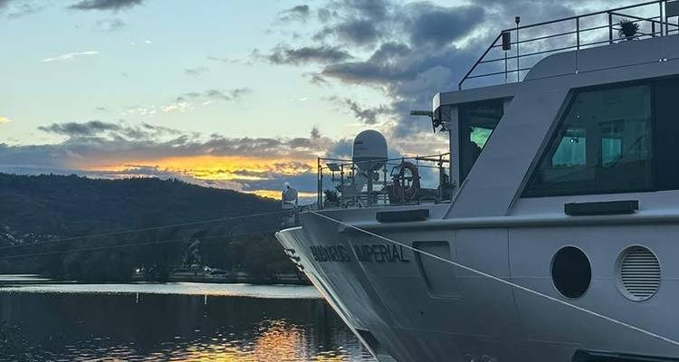 Rivierboot bij zonsondergang met een achtergrond van heuvels, wat een serene tafereel creëert.