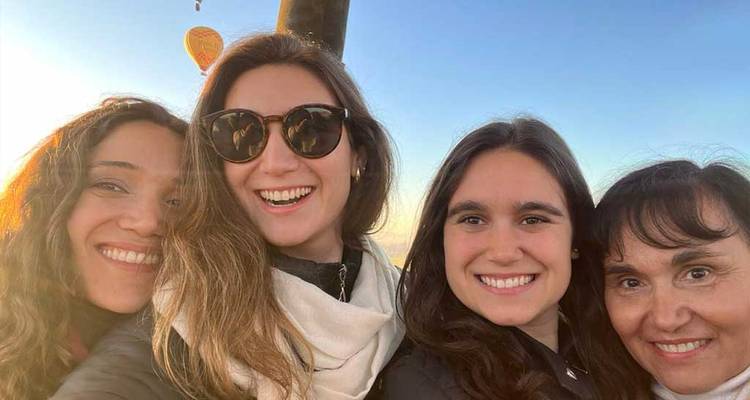 Quatre femmes heureuses posent avec une montgolfière au lever du soleil flottant derrière elles.