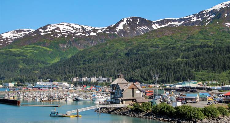 Marina en Whittier con barcos, paisaje alpino de fondo y picos nevados en un día soleado.