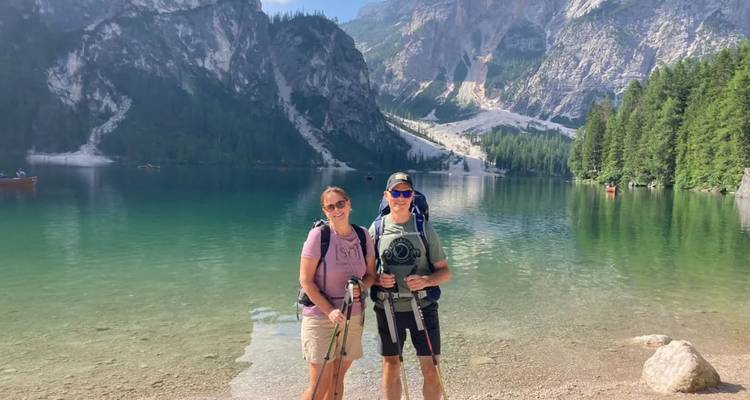 Couple avec des bâtons de randonnée debout dans l'eau peu profonde d'un lac alpin cristallin avec des falaises derrière.