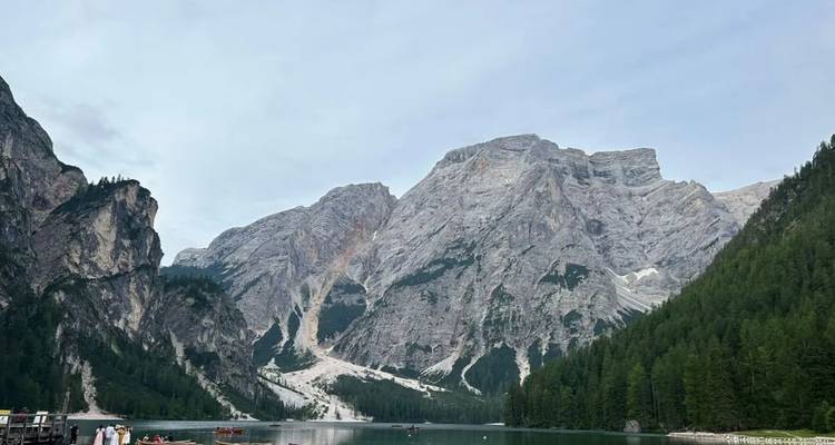 Vue large d'un lac vert et calme entouré de montagnes escarpées et boisées sous un ciel gris.