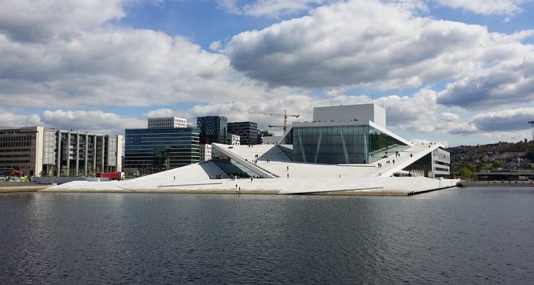 Opéra moderne d'Oslo en marbre blanc s'élevant du port avec des reflets sous un ciel partiellement nuageux.