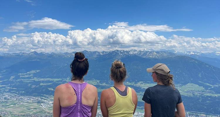 Trois randonneurs photographiés de dos admirant un vaste panorama montagneux et des nuages.
